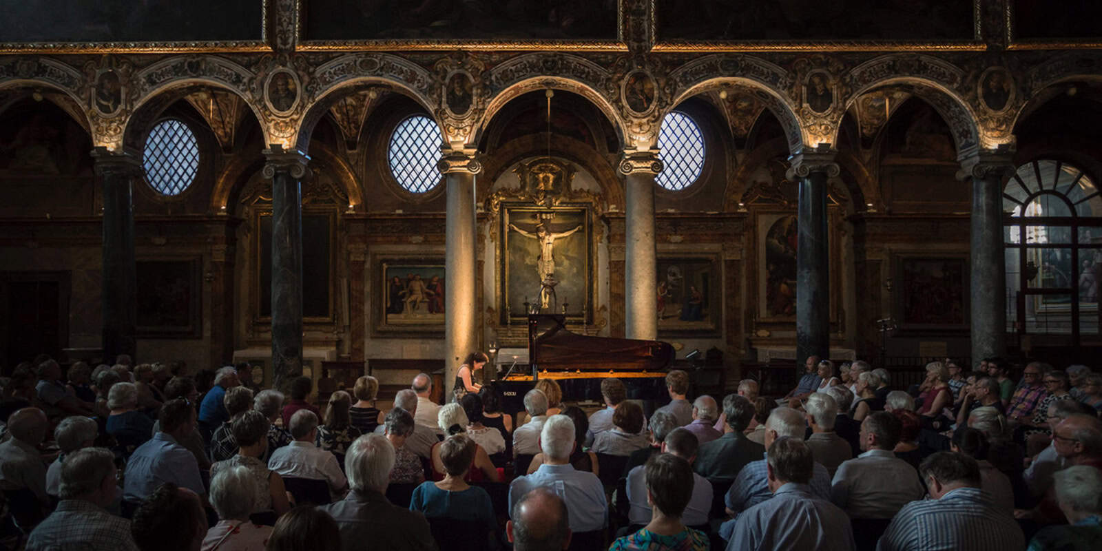 Eine Gruppe von Menschen, die in einer Kirche einer Frau zuhören, die Klavier spielt.